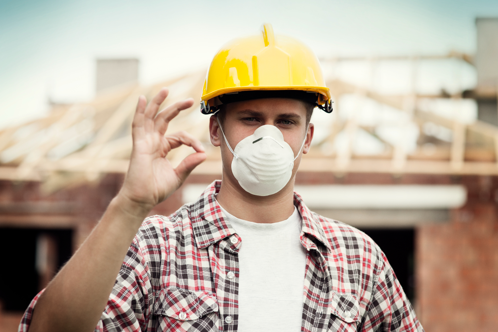 Construction site worker wearing a face mask and making an OK sign with his hands.