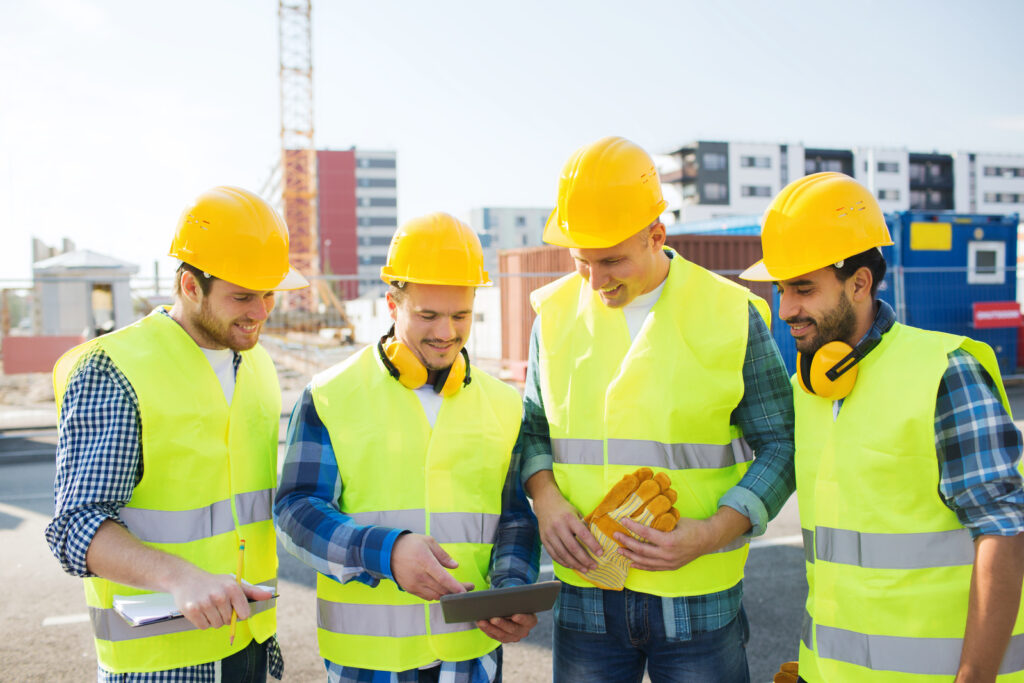 Group of four construction workers on site looking at a tablet during a training session.