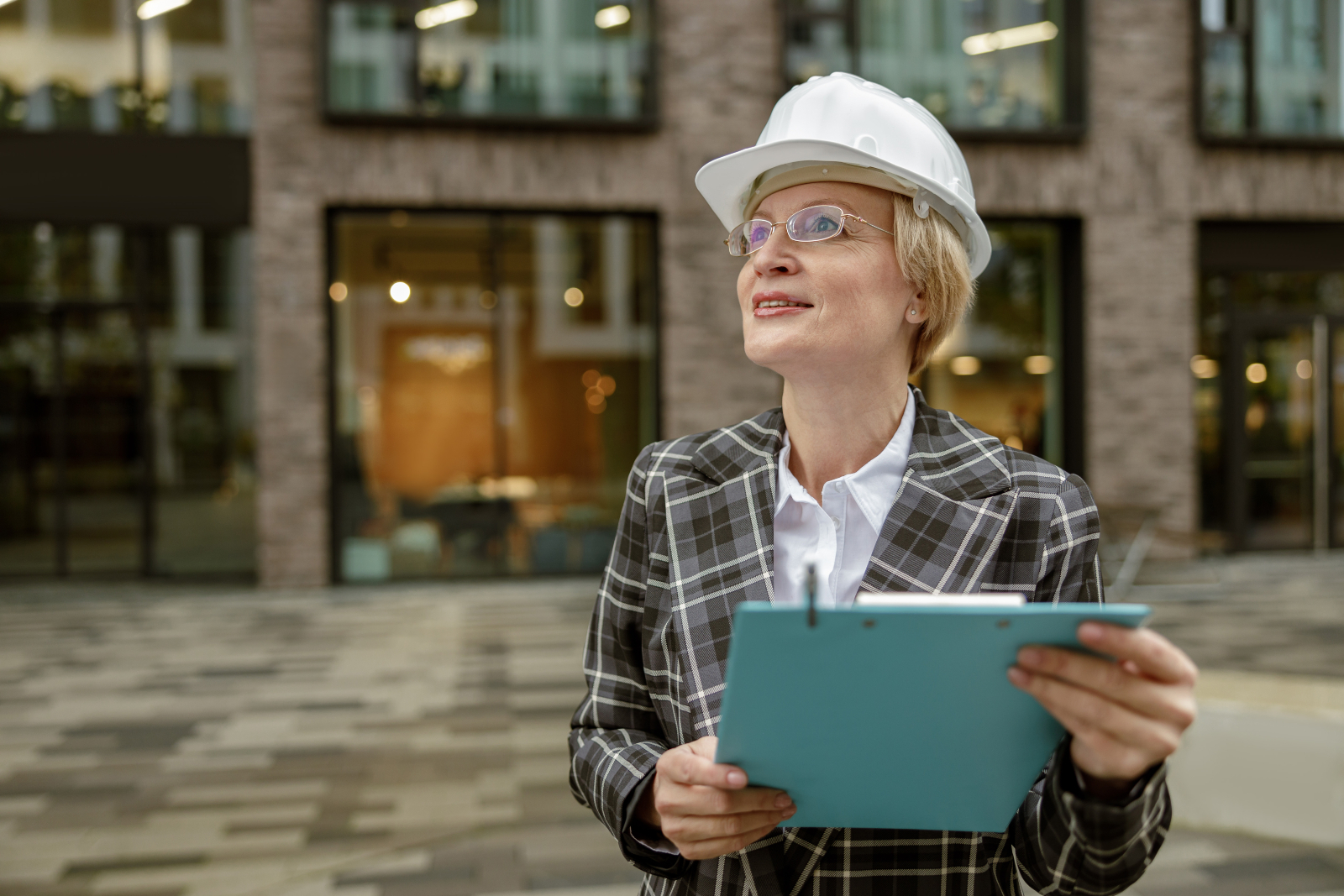 Image of a female building inspector with a clipboard standing in front of a city building.