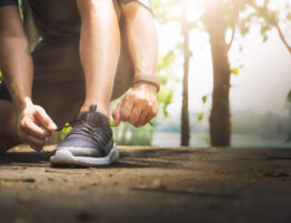 Image showing someone's leg and foot as they lace up their trainer with a blurred forest in the background