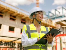 Woman on a construction site wearing a high vis jacket and hard hat and holding a clip board