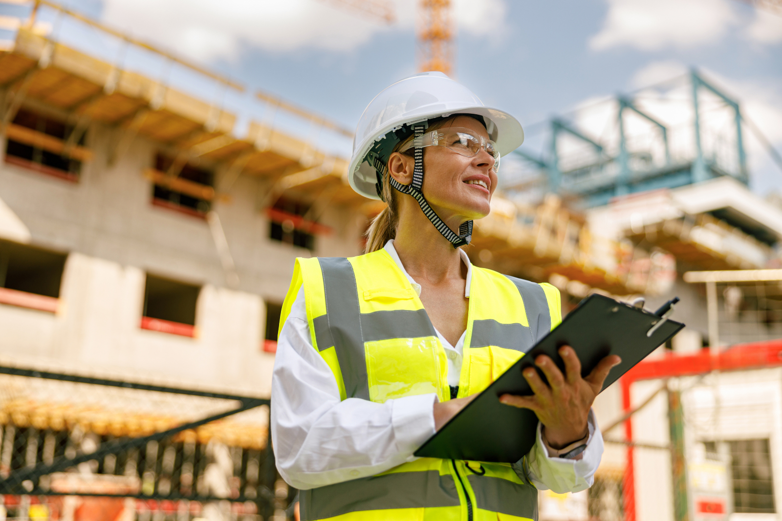 Woman on a construction site wearing a high vis jacket and hard hat and holding a clip board