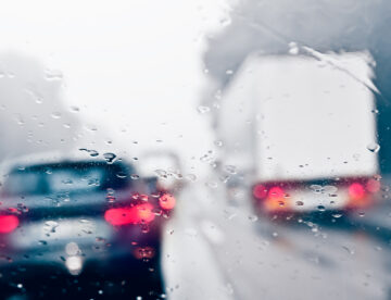 Image showing some cars and a van driving on a road in rainy conditions. The image is blurred due to water on the camera lens.