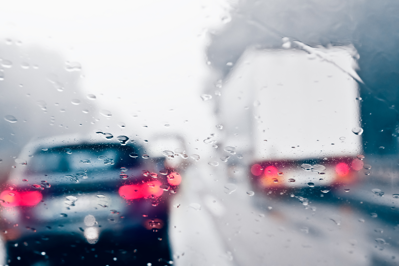 Image showing some cars and a van driving on a road in rainy conditions. The image is blurred due to water on the camera lens.