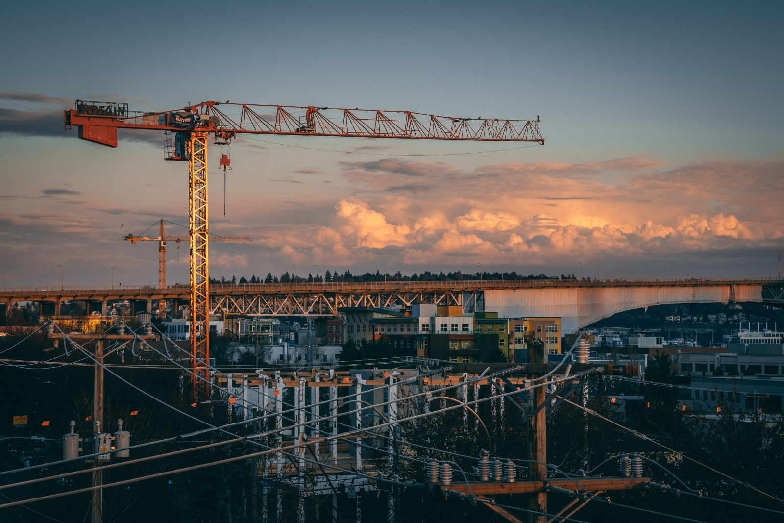 Aerial image showing a construction site with several buildings and a crane set against a darkening evening sky