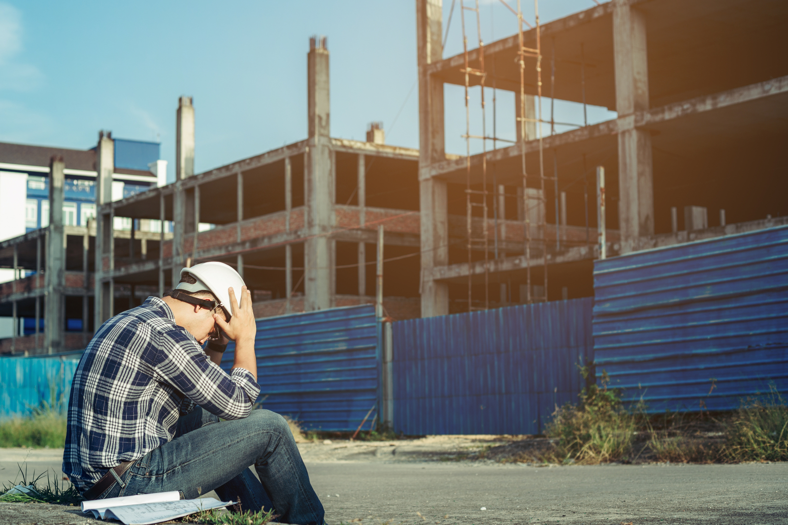 Image of a man on a construction site, sitting down with his head in his hands, looking stressed.