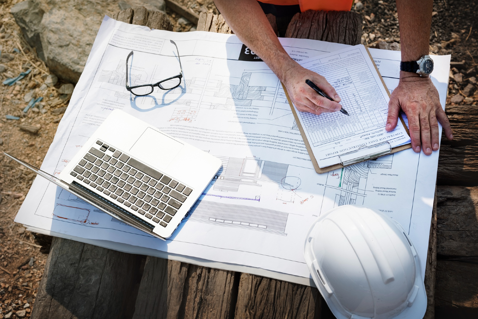 Image showing various items laid out on a table - construction plans, a laptop, a clipboard, glasses and a safety helmet