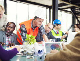 Image showing a diverse construction team working collaboratively around a table, some looking documents and IT equipment.