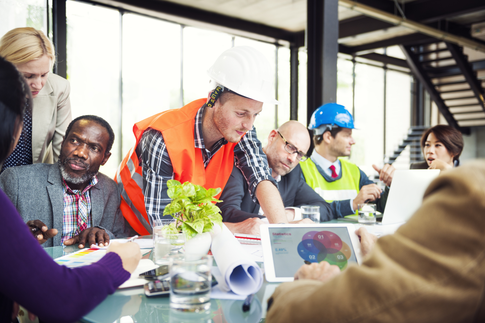 Image showing a diverse construction team working collaboratively around a table, some looking documents and IT equipment.