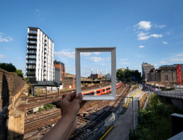 Image showing someone holding up a photo frame in front of a trainline and buildings in the background