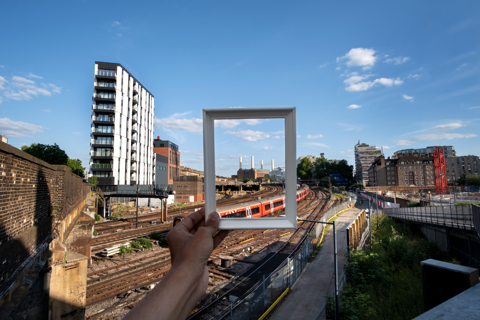 Image showing someone holding up a photo frame in front of a trainline and buildings in the background