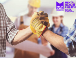 Close up of two construction workers arms (with hands shaking) with other workers standing behind them. Also featuring the Mental Health Awareness Week logo.