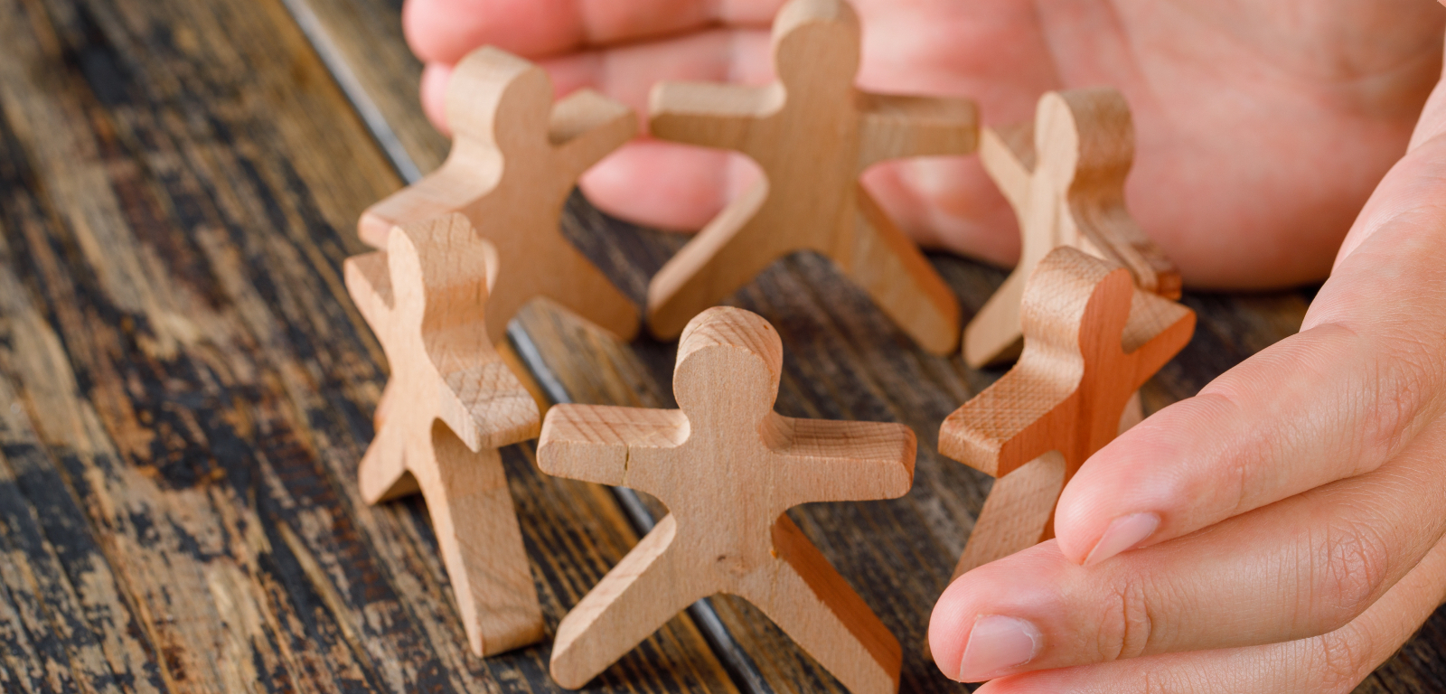 Woman's hands around small wooden figures of people in a circle