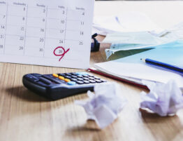 Close up of a work desk with a calendar (with a date circled) plus a calculator and scrap paper