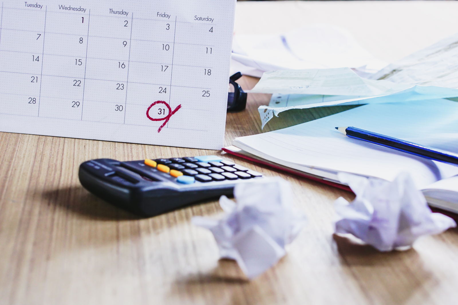 Close up of a work desk with a calendar (with a date circled) plus a calculator and scrap paper