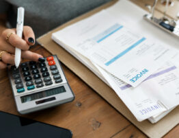 Accounting concept featuring a close up of a woman's hands using a calculator next to a file of invoices