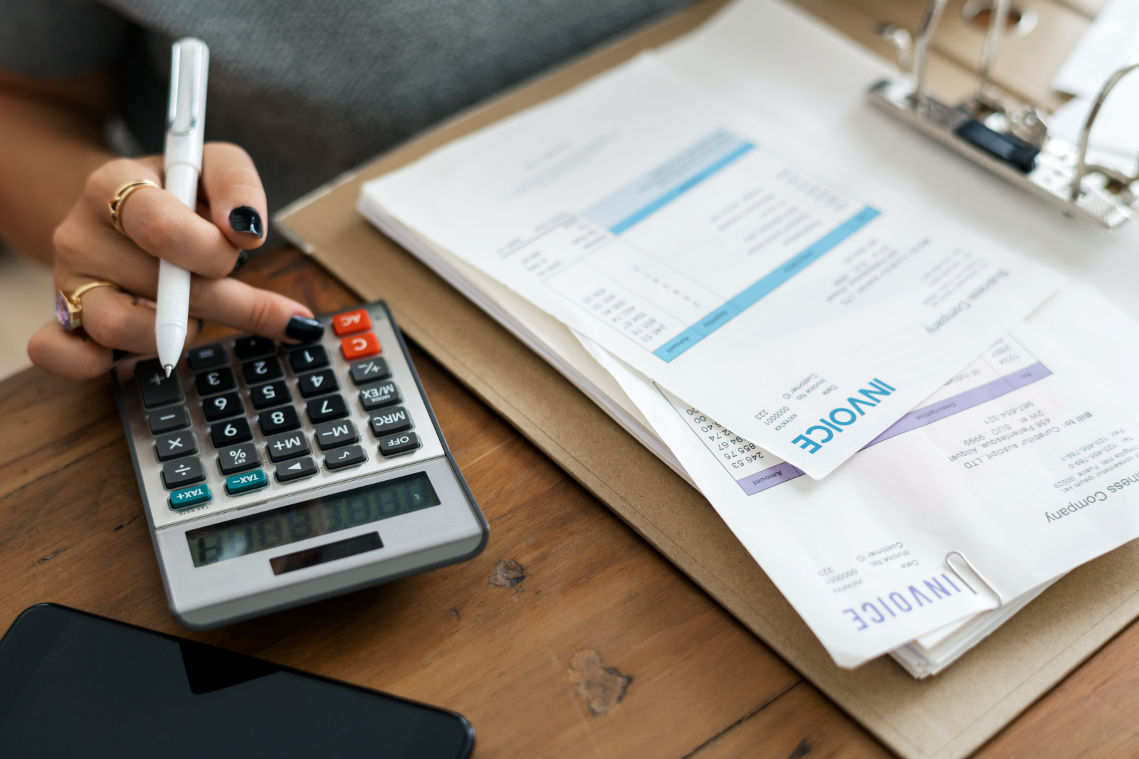 Accounting concept featuring a close up of a woman's hands using a calculator next to a file of invoices