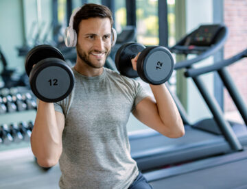 Man in a gym wearing headphones and lifting dumbbells to shoulders