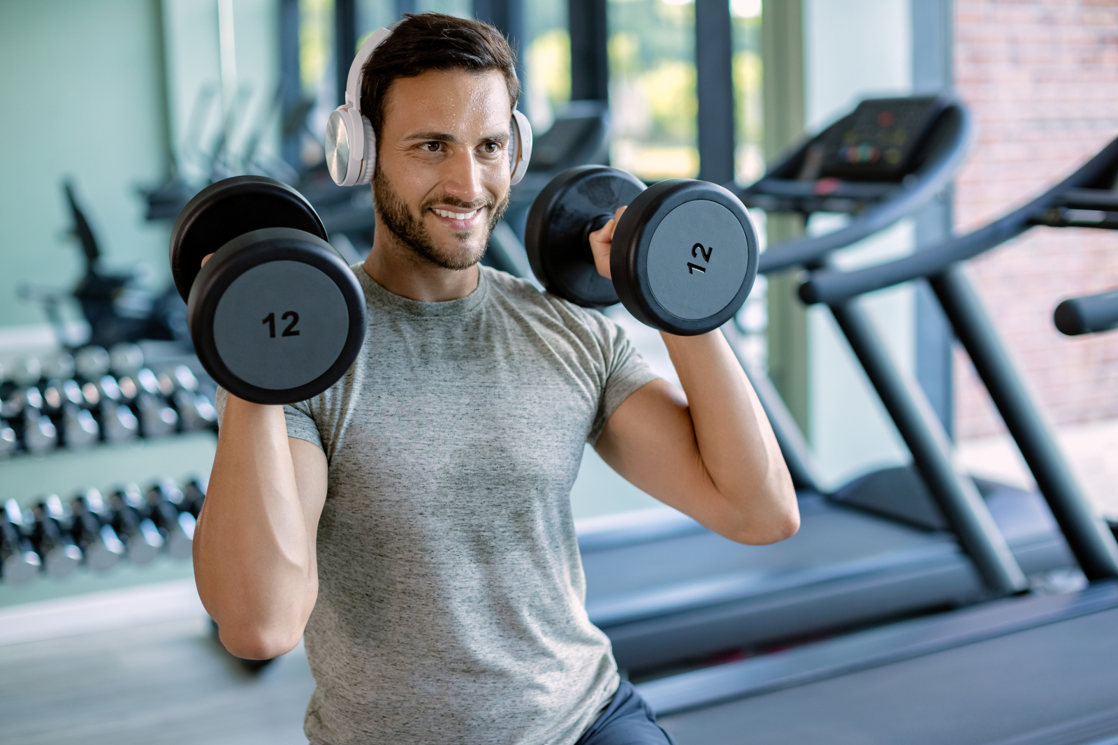 Man in a gym wearing headphones and lifting dumbbells to shoulders