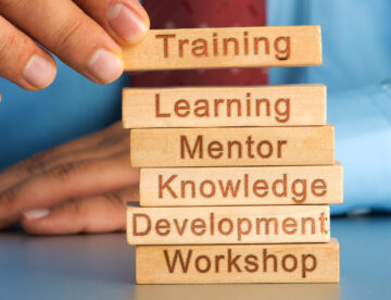 Close up of someone placing small wooden blocks into a tower shape with each block featuring words like training, learning and development