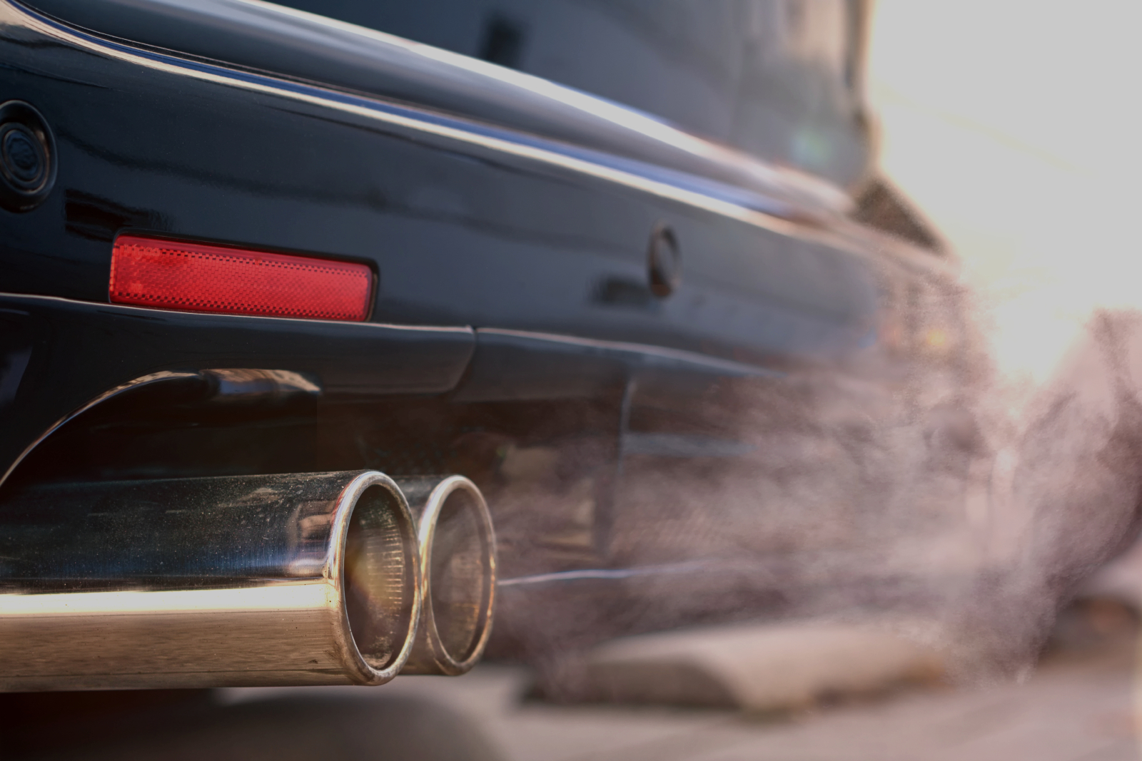 Close up of rear end of a car showing the exhaust emitting fumes