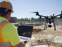 Construction worker on site using a drone and looking at a laptop, representing technology-related careers in construction