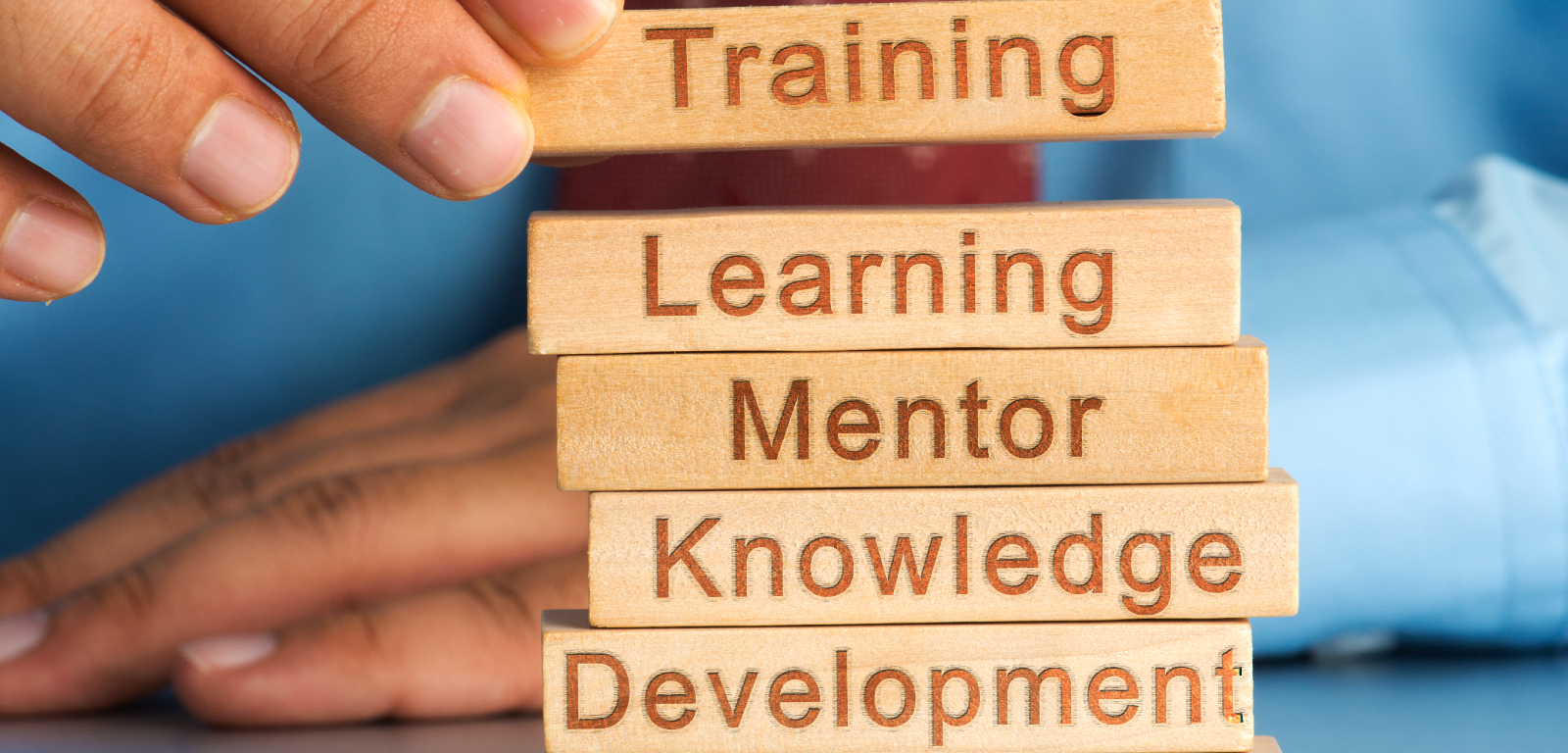 Close up of someone placing small wooden blocks into a tower shape with each block featuring words like training, learning and development