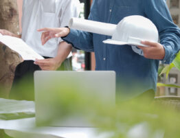 Construction team looking at plans and a laptop. The image only shows the mid-section of the team and there is a green hue to the forefront
