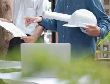 Construction team looking at plans and a laptop. The image only shows the mid-section of the team and there is a green hue to the forefront