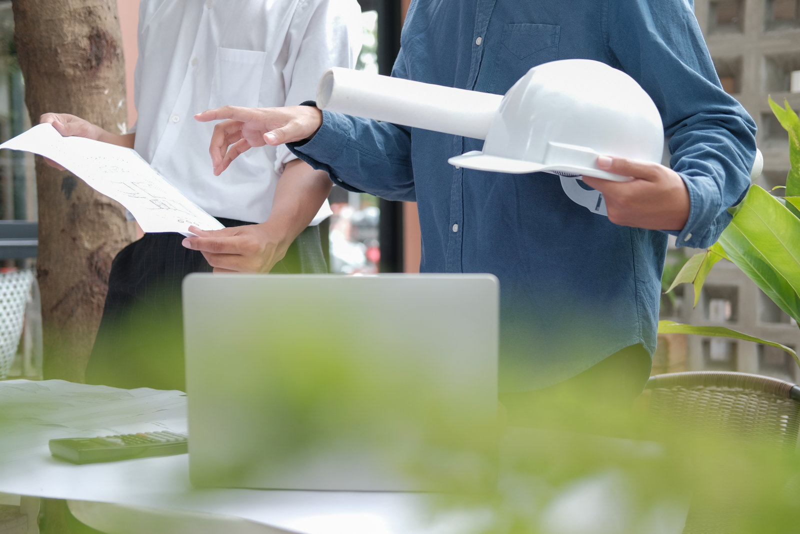 Construction team looking at plans and a laptop. The image only shows the mid-section of the team and there is a green hue to the forefront