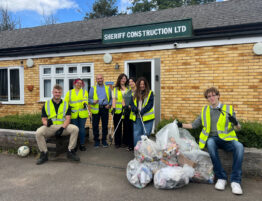 Eight members of Sheriff Construction staff standing outside the office in high vis jackets with bags of litter in front of them