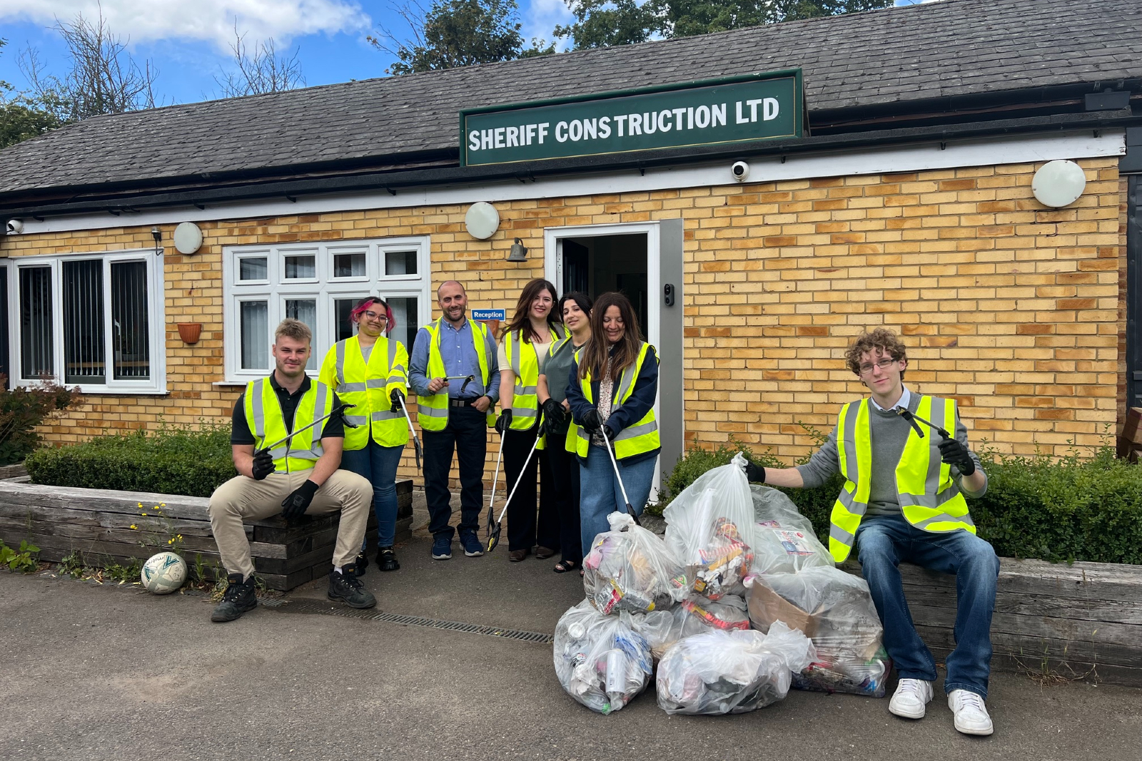 Eight members of Sheriff Construction staff standing outside the office in high vis jackets with bags of litter in front of them