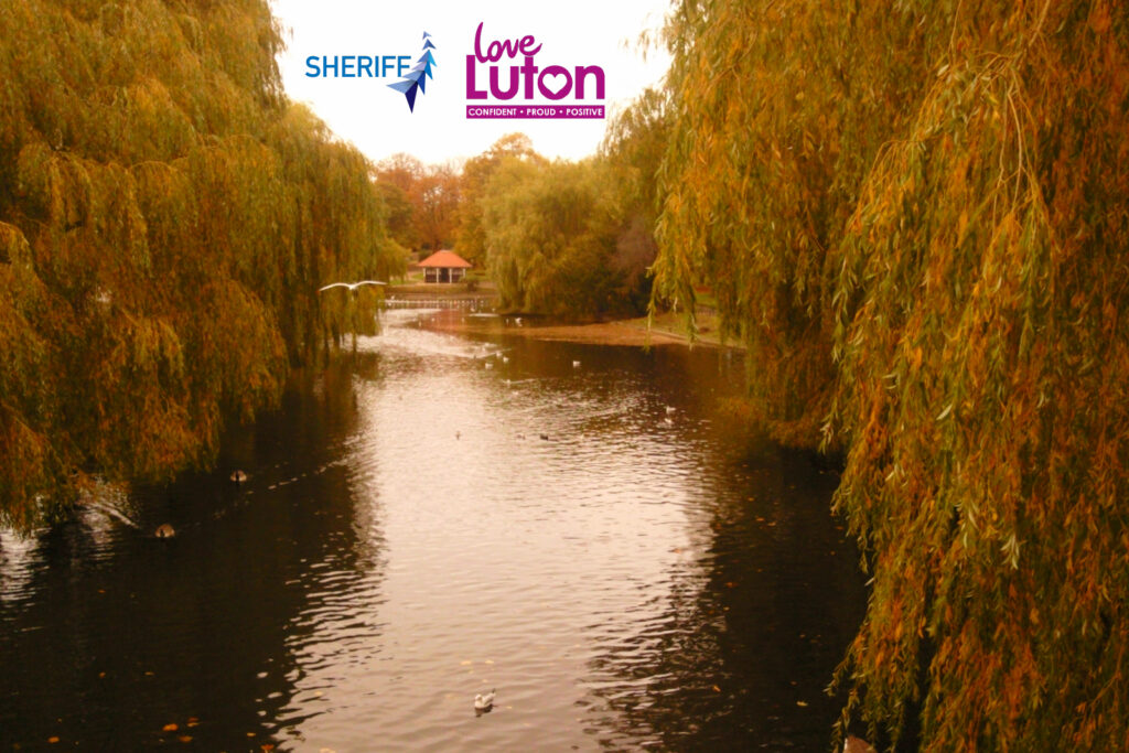 Wardown park in Luton showing the River Lea and a bronze hue. Logos for Sheriff Construction and Love Luton also feature