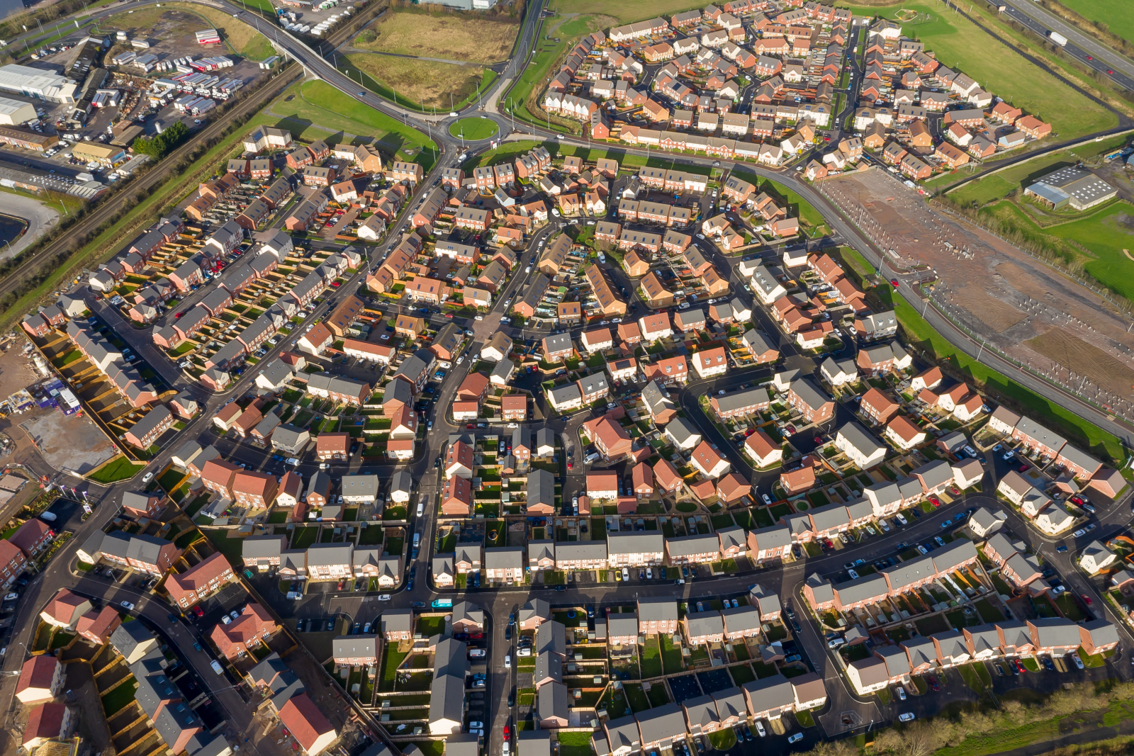 Aerial shot of a housing development in England with roads and a roundabout clearly visible. Some signs of new development appear at the edges of the image.