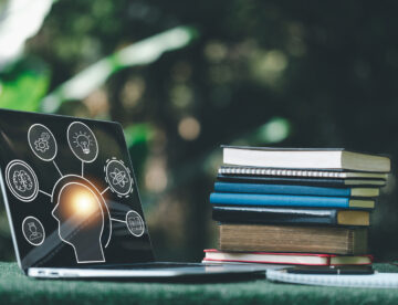 Table with a pile of books and a laptop with graphics on it relating to the brain and learning (e.g. a lightbulb).