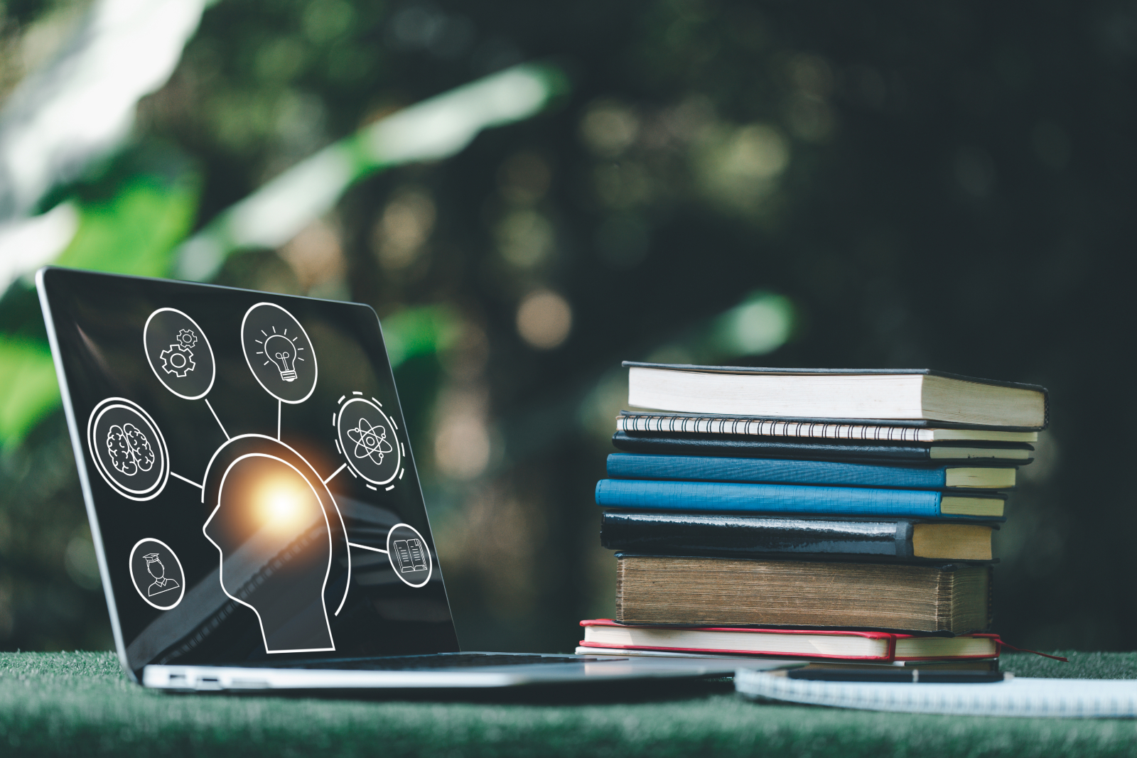 Table with a pile of books and a laptop with graphics on it relating to the brain and learning (e.g. a lightbulb).
