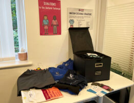 Collection box filled with school uniform items plus further uniform pieces on a table. Leaflets and posters about The Level Trust are also featured in the image.
