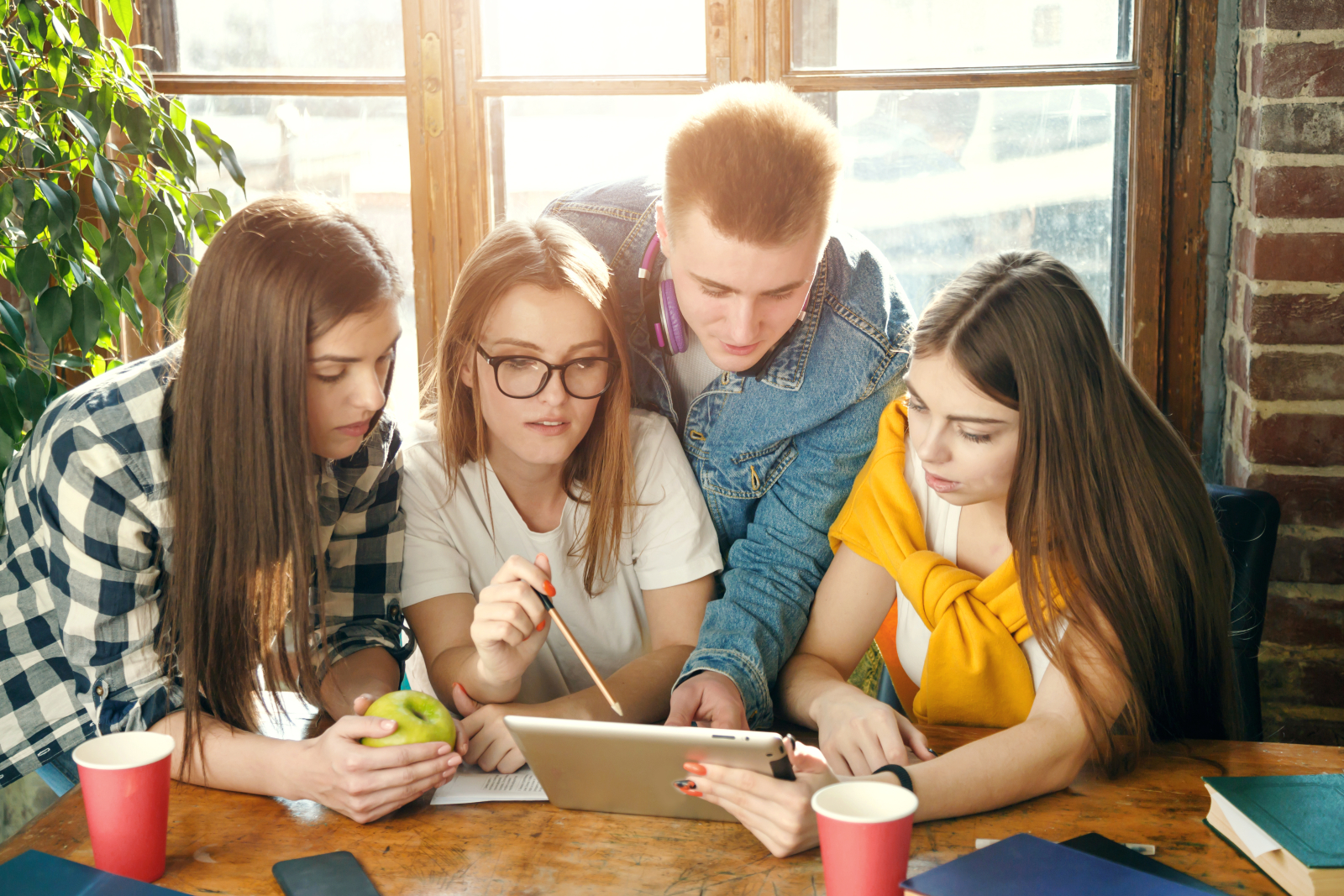 Four young people sat at a table, looking at a laptop with the suggestion they are having a discussion.